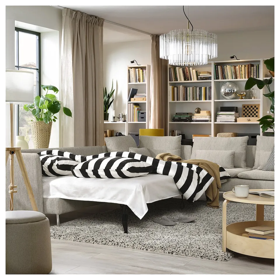 Modern living room with SÖDERHAMN sofa bed, striped pillows, coffee table, bookshelves, chandelier, and plants.