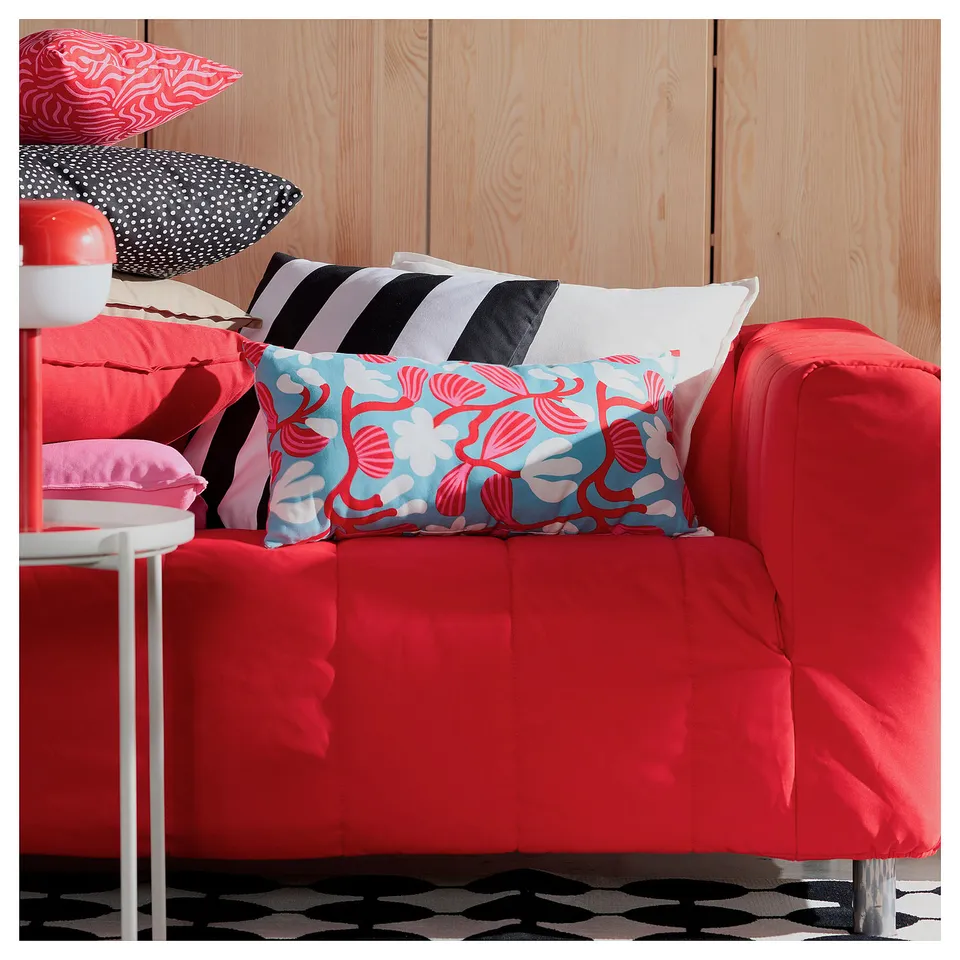 Bright red couch with colourful floral pillows against wooden wall.