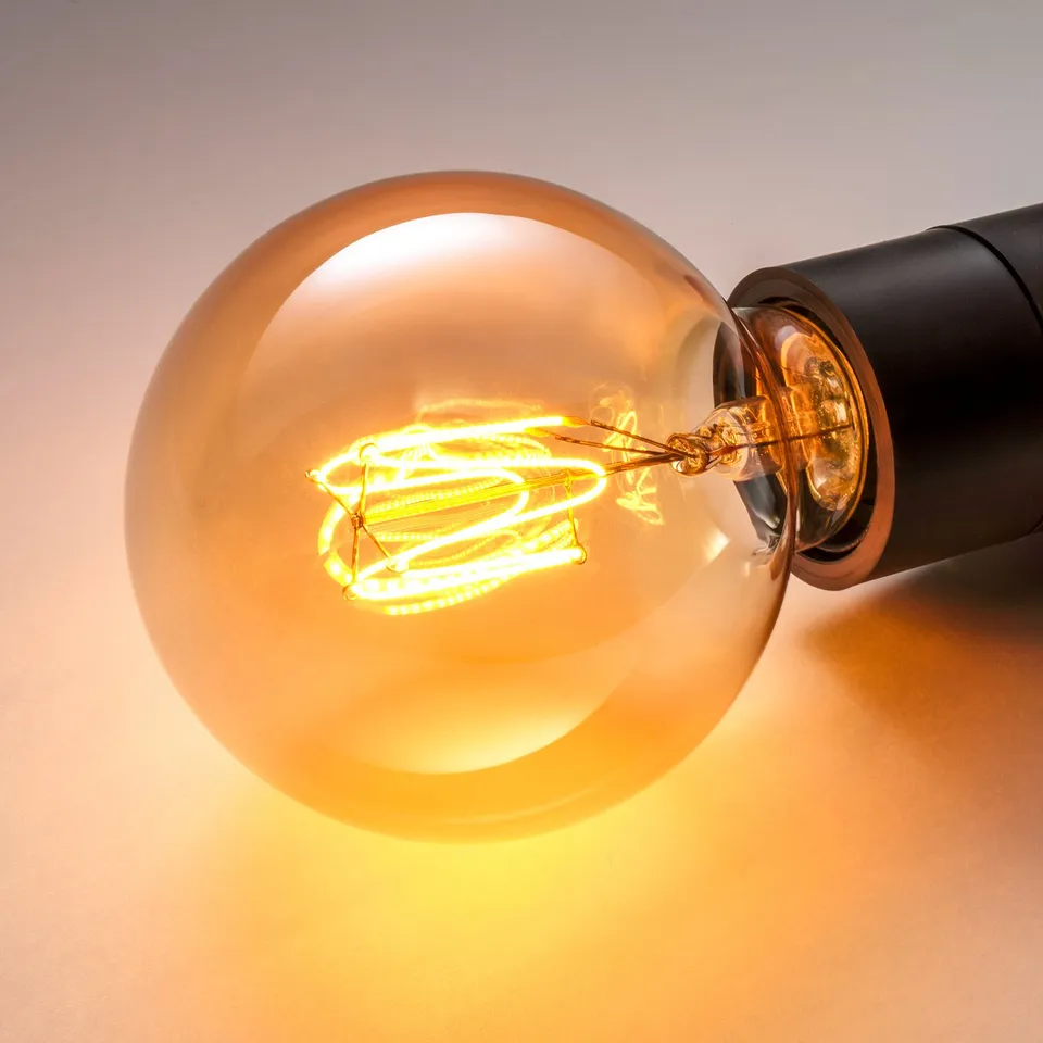 Close-up of a warm, glowing light bulb. Amber glass emits soft, inviting light, creating a cosy atmosphere.