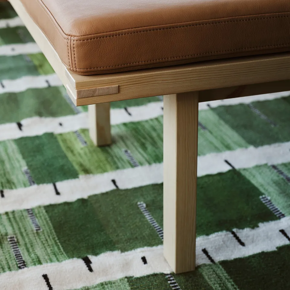 Brown leather-cushioned bench with wooden legs on a green and white patterned rug.
