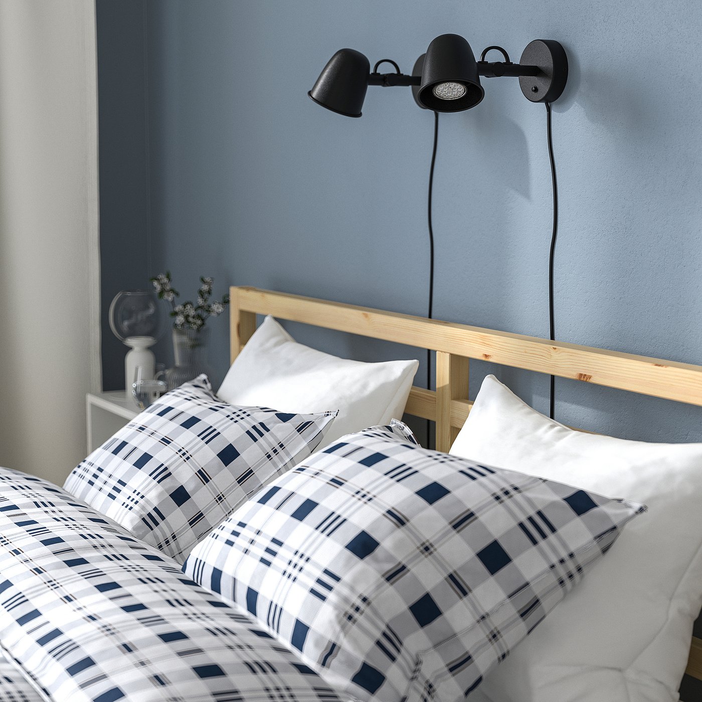 A cosy, modern bed with a wooden headboard, plaid duvet, and wall-mounted bedside lamps.