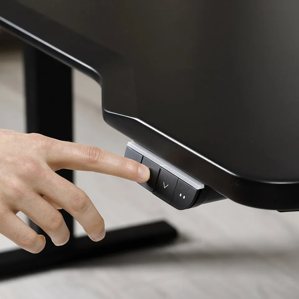 Hand adjusts electric standing desks control panel, showcasing sleek, durable design with modern finish.