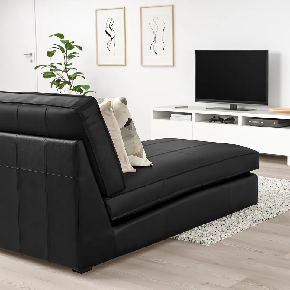 Modern living room with large black KIVIK chaise, flat-screen tv, white console, decorative plant, rug, and minimalist art.
