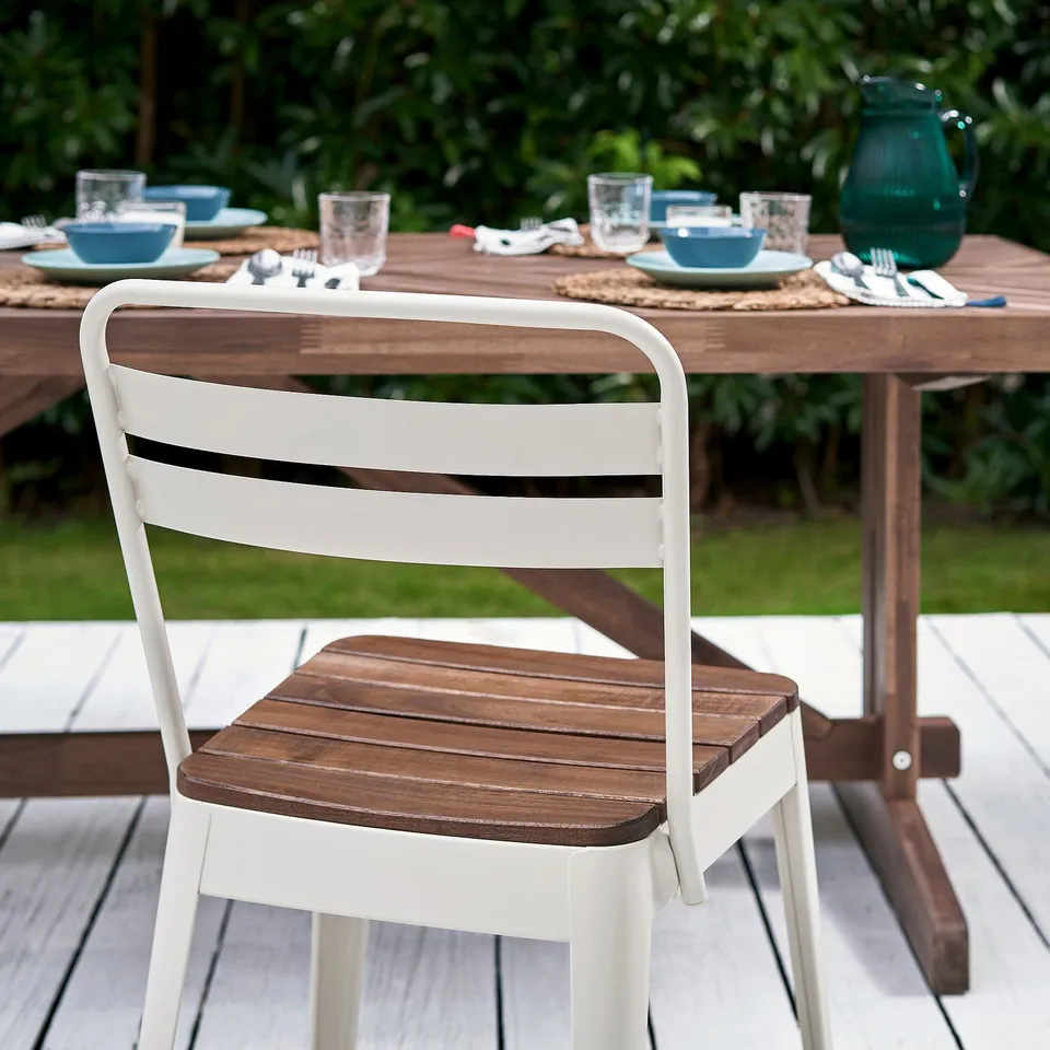 Outdoor dining setup with white norrmanso chair, wooden table, plates, and glasses.