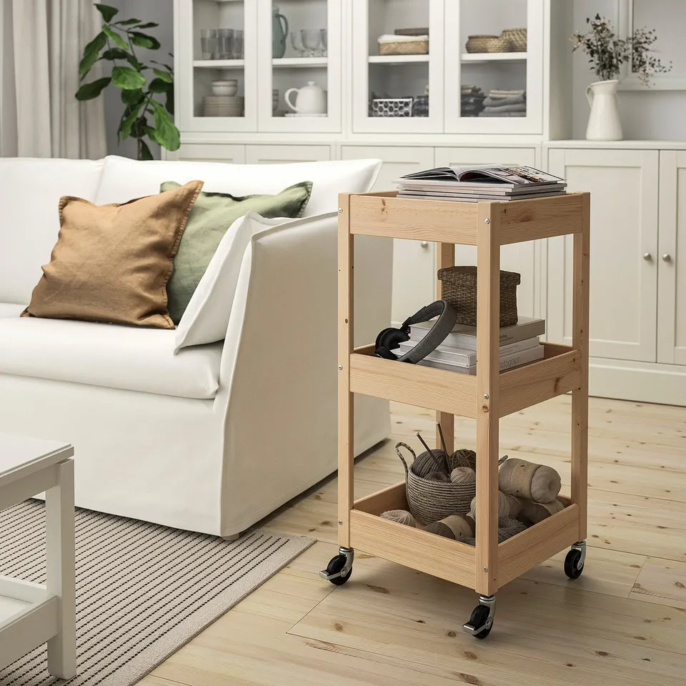 Wooden storage trolley with books, baskets, yarn beside a couch.