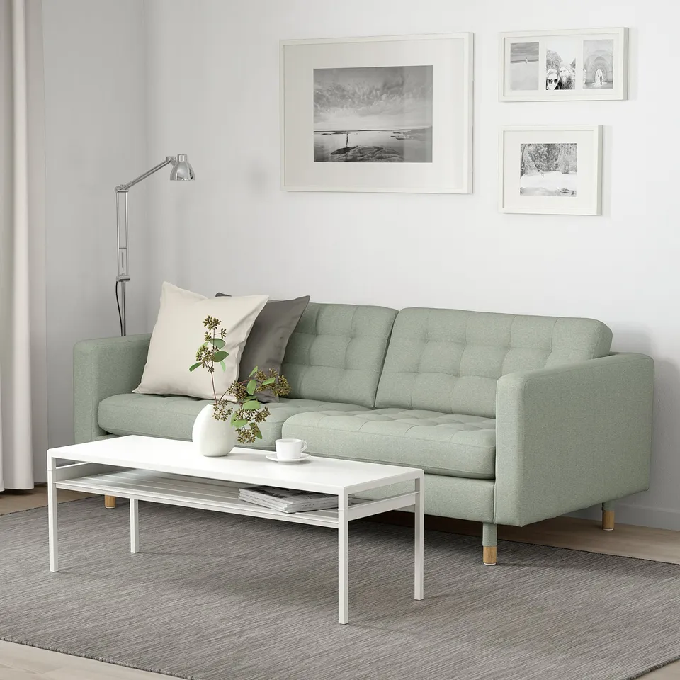 Cosy living room with mint green sofa, white coffee table, and floral vase. Modern minimalist decor with black and white wall photos.