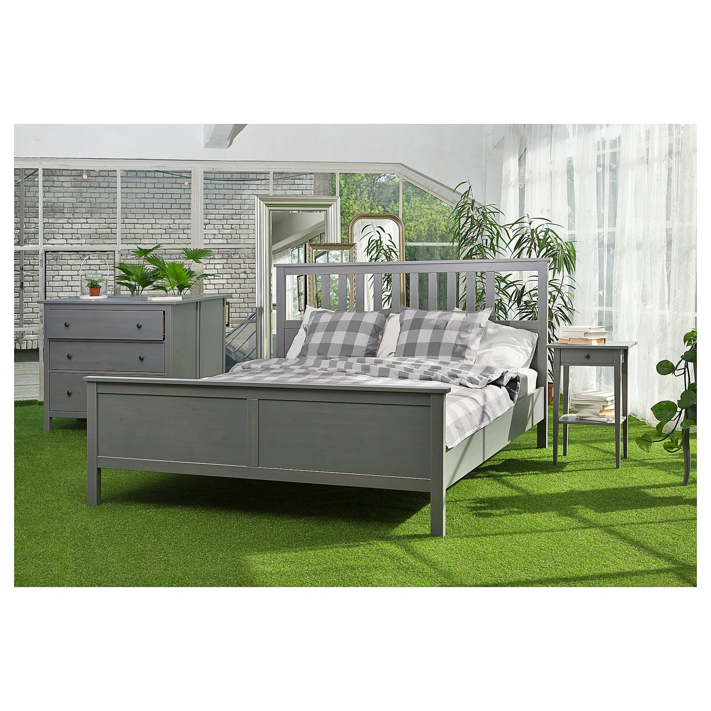 Bedroom setup with grey HEMNES bed, dresser, and table on artificial green turf indoors.