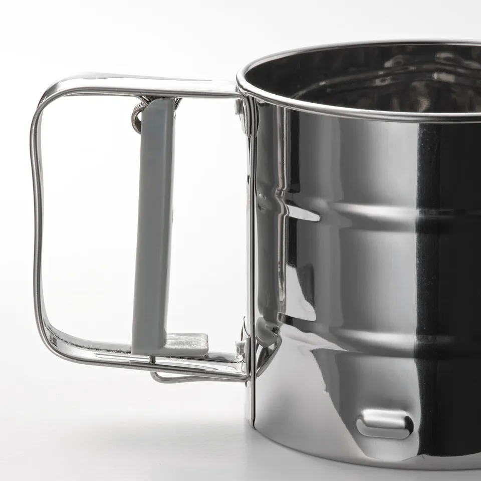 Shiny metal cup with sturdy handle, reflecting light, on plain white surface.