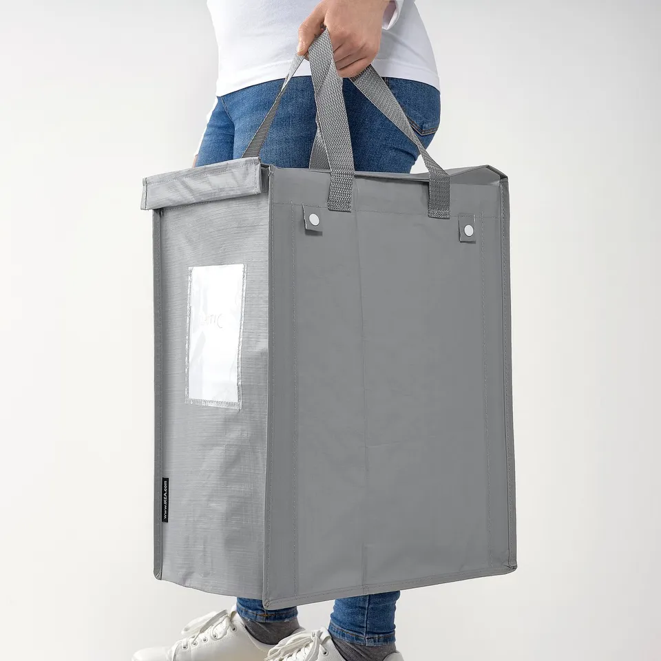 Person holding a large grey DIMPA waste-sorting bag with side handles and a transparent pocket.
