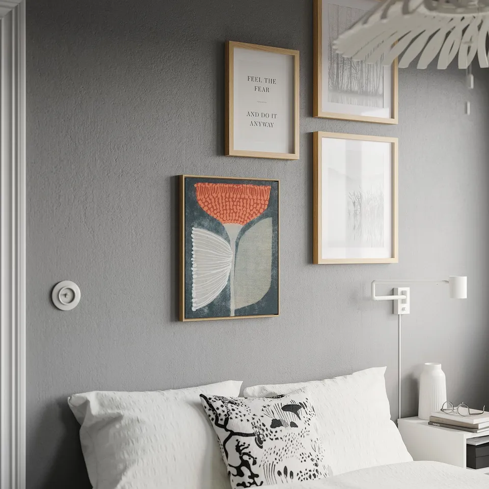 Wall with BLODFLÄDER poster, colourful canvas above bed, black-white prints, wall light, bedside decor.