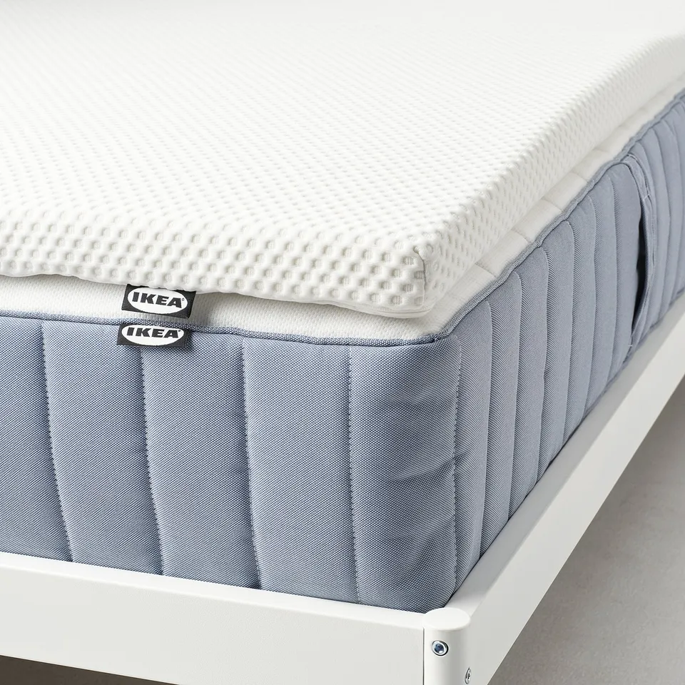 Ikea mattress pad with memory foam, offering pressure relief and a cozy feel, displayed on a white frame.