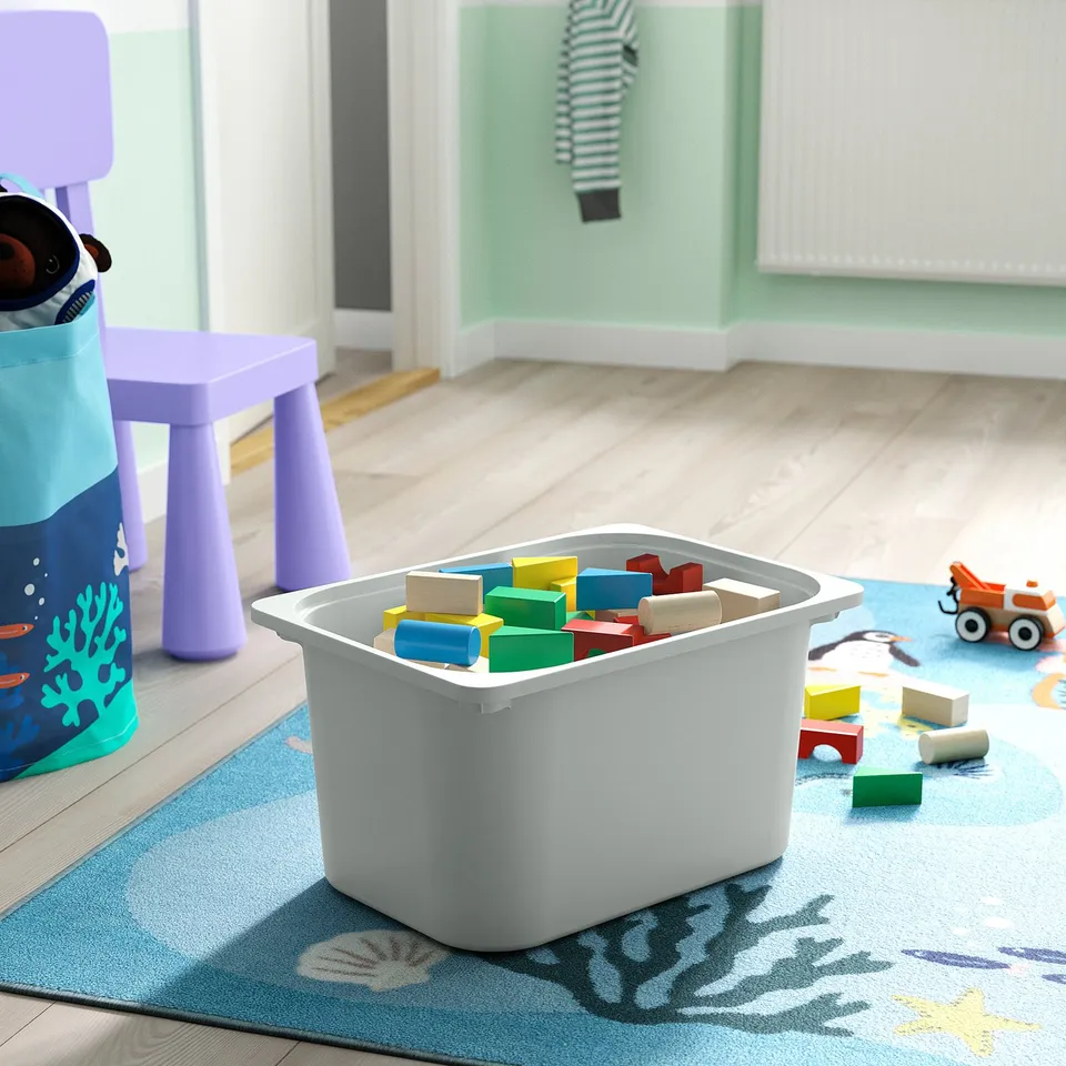 White plastic storage bin filled with colourful wooden blocks, on a blue rug with a sea theme, placed in a childs playroom.