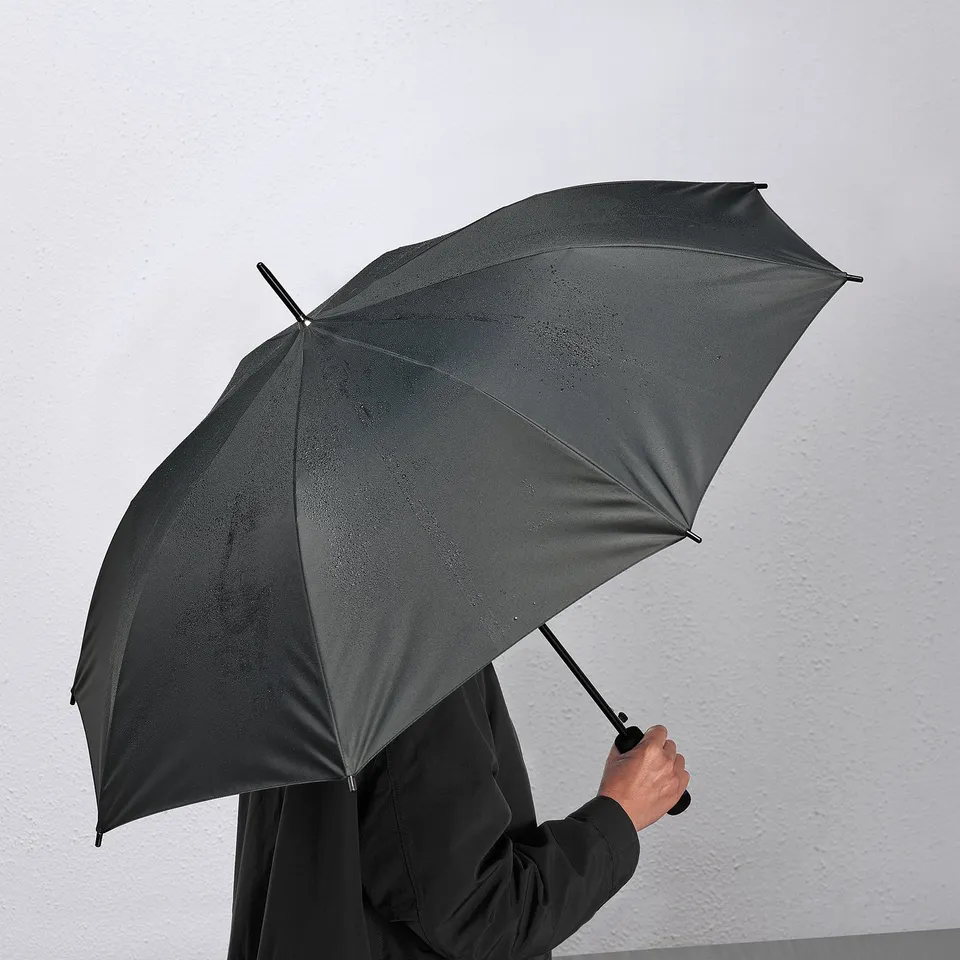 Person holding large, black automatic umbrella indoors, ready for rain.
