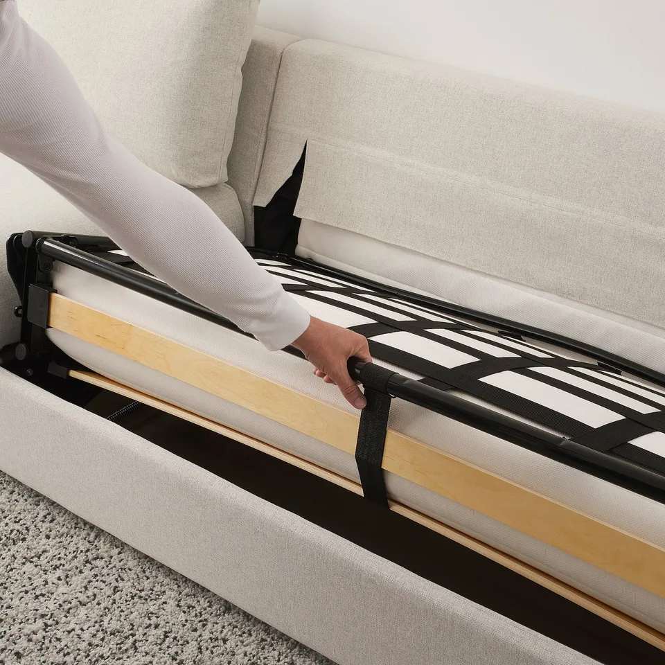 Person adjusts sofa-bed mechanism, converting sofa to bed. Streamlined metal frame visible.