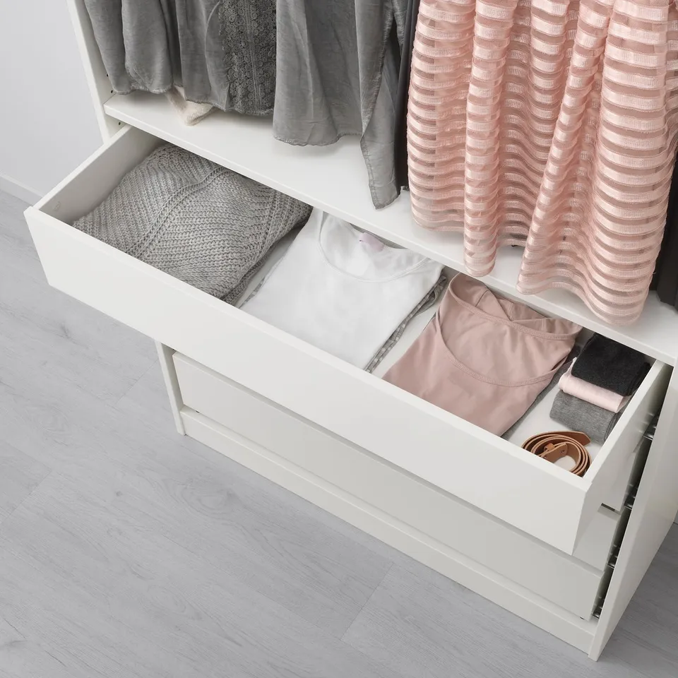 Open white wardrobe drawer showing organised clothes and accessories, including folded sweaters and grey socks, demonstrating storage efficiency.