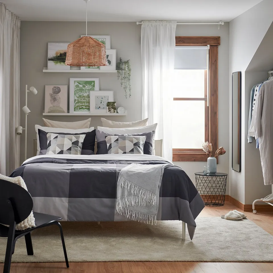 Modern bedroom with grey bedding, patterned pillows, and a pendant light. Central bed, left chair, right side table.
