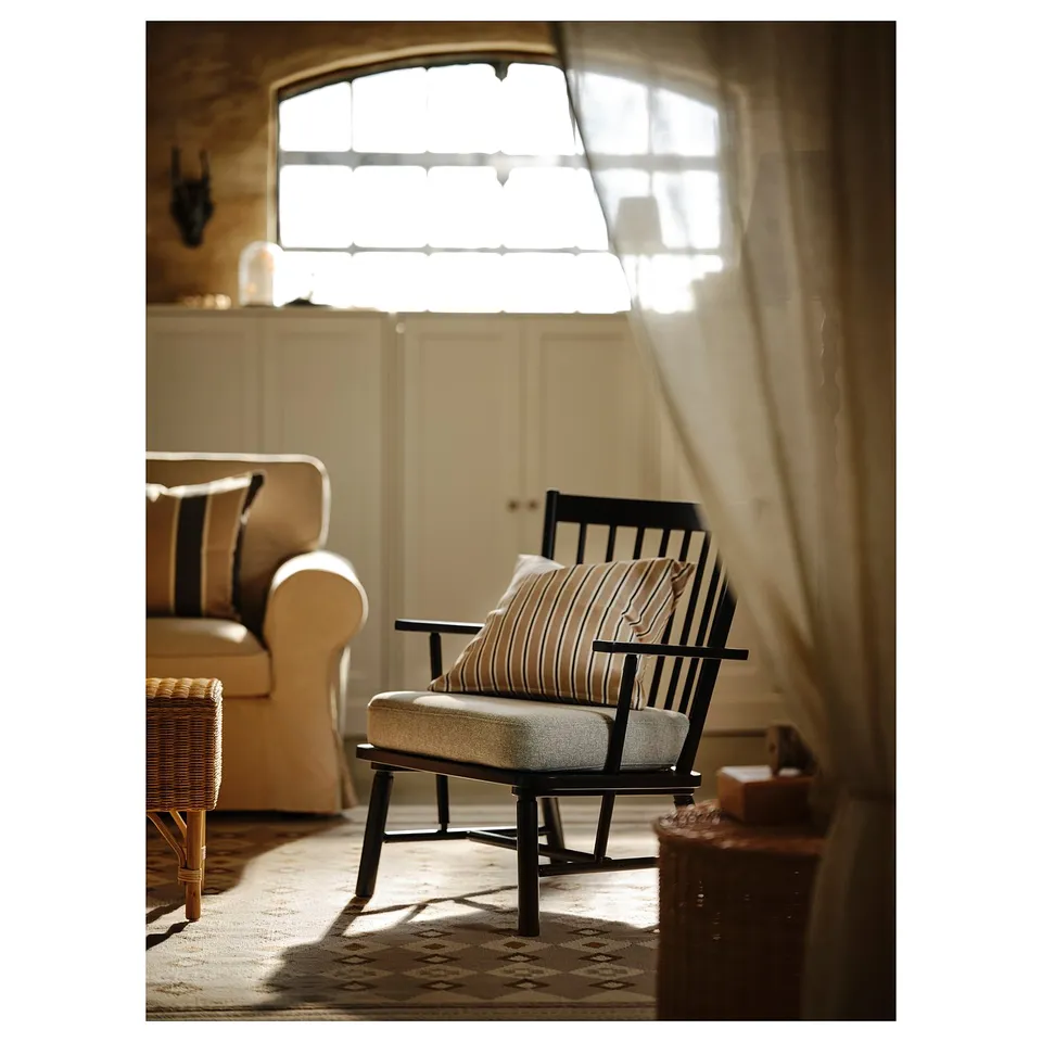 Cosy living room with black rocking chair, striped cushions. Sunlight through arched window warms sofa and rug.