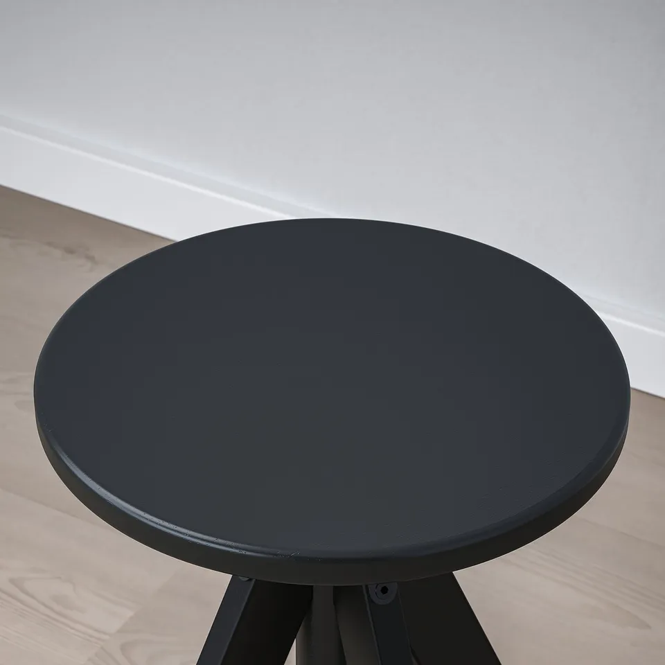 A modern, round stool with a smooth black seat on a sturdy wooden leg, perfect for any space.
