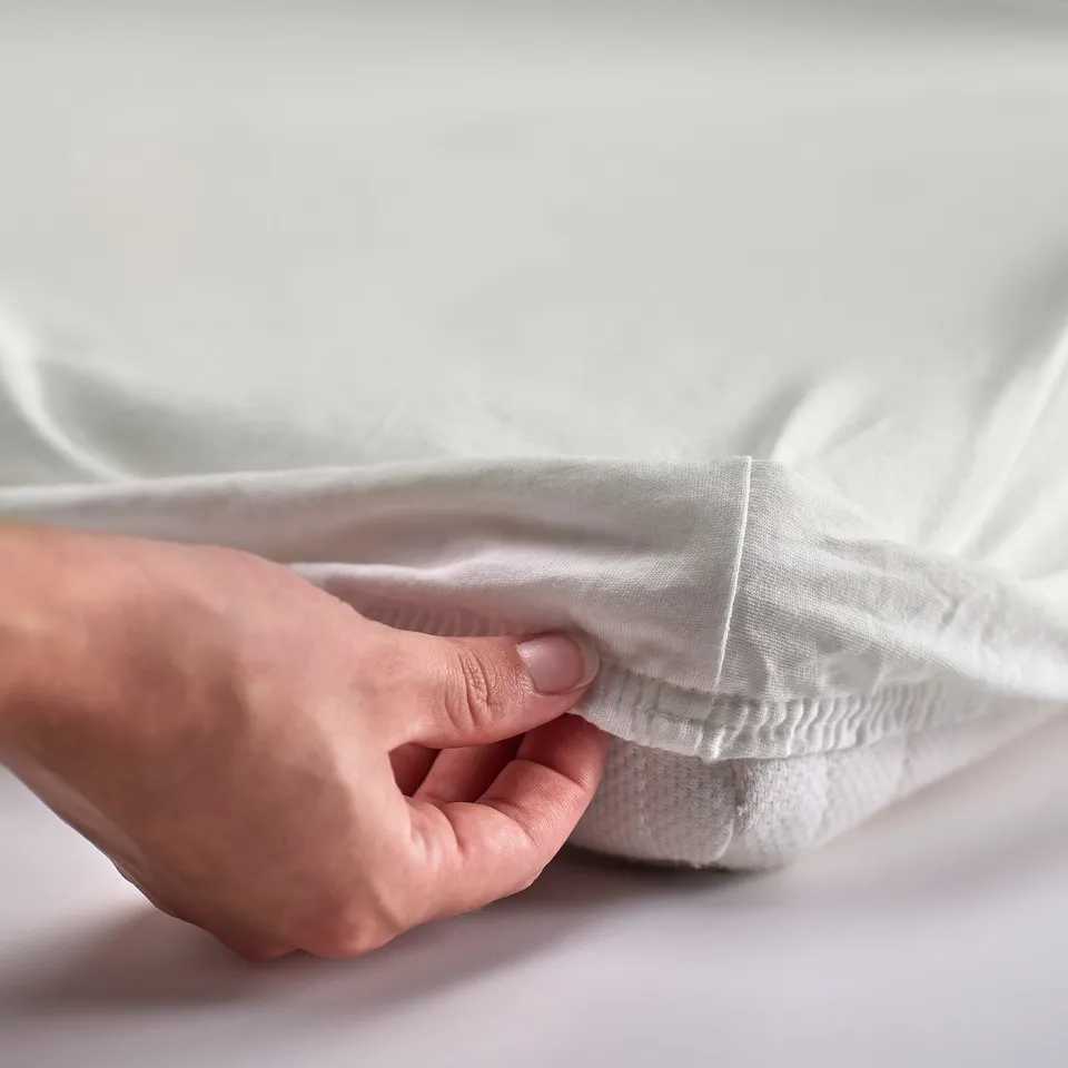 A hand holding a white LEN fabric edge, showcasing its texture and stitching.