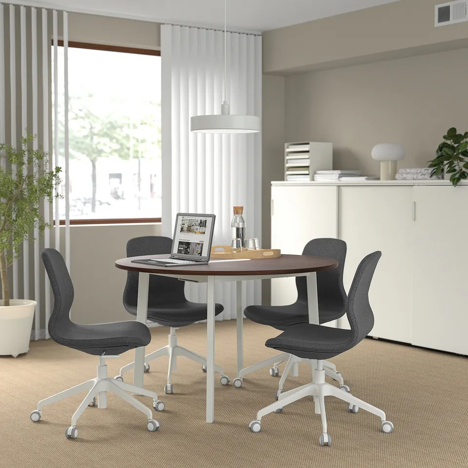 Modern minimalist meeting area with MITTZON table, dark chairs, white cabinet, large window, and plants.