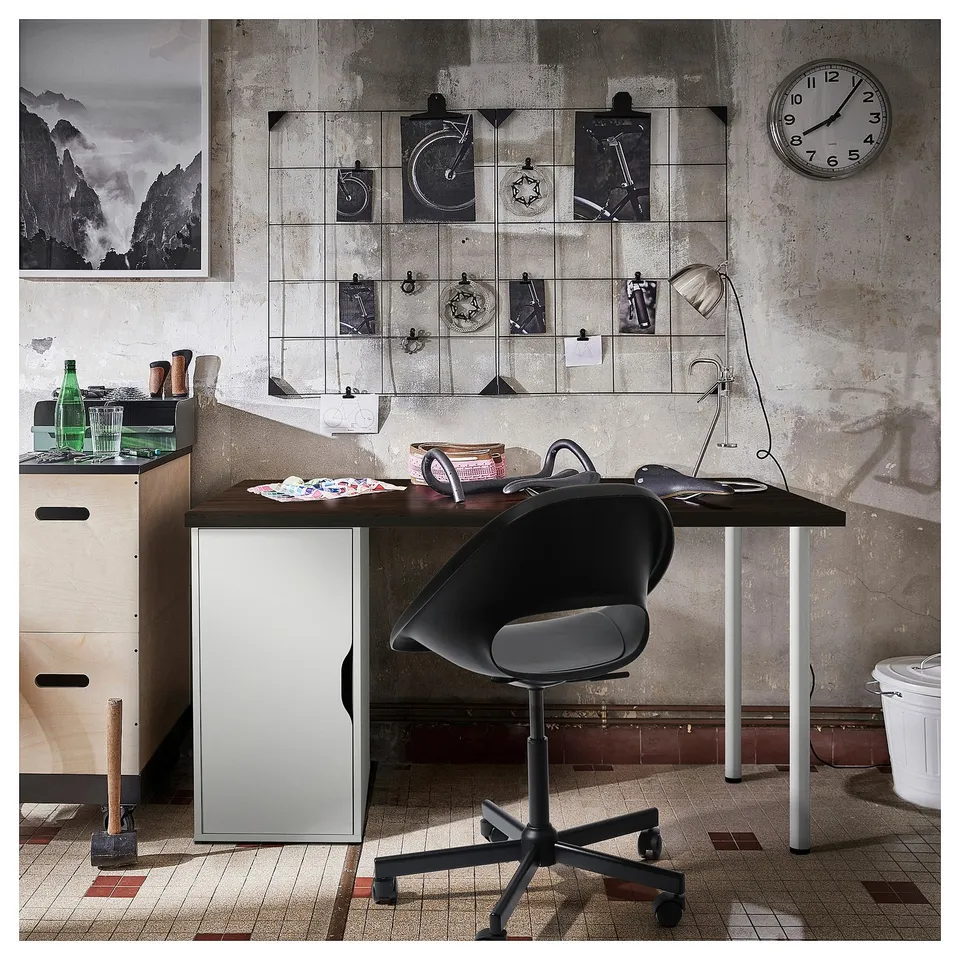 Modern industrial desk setup with black chair, glass lamp, and wall decor including a clock and photos.