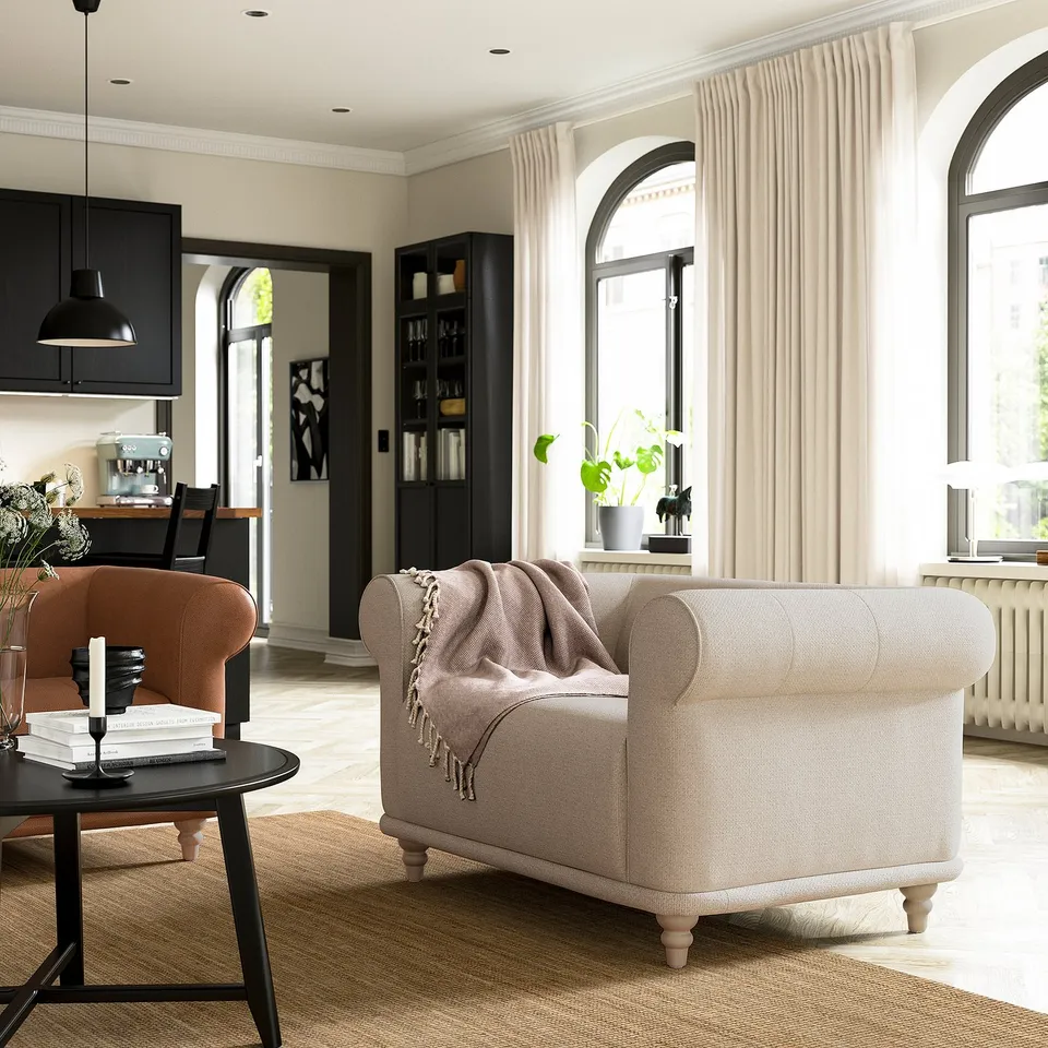Elegant living room: beige VISKAFORS armchair with blanket, orange side chair, black coffee table, arched windows, curtains, and dark wood accents.