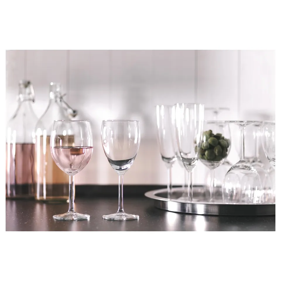 Clear wine glasses on shiny black surface, surrounded by clear bottle and green grapes.