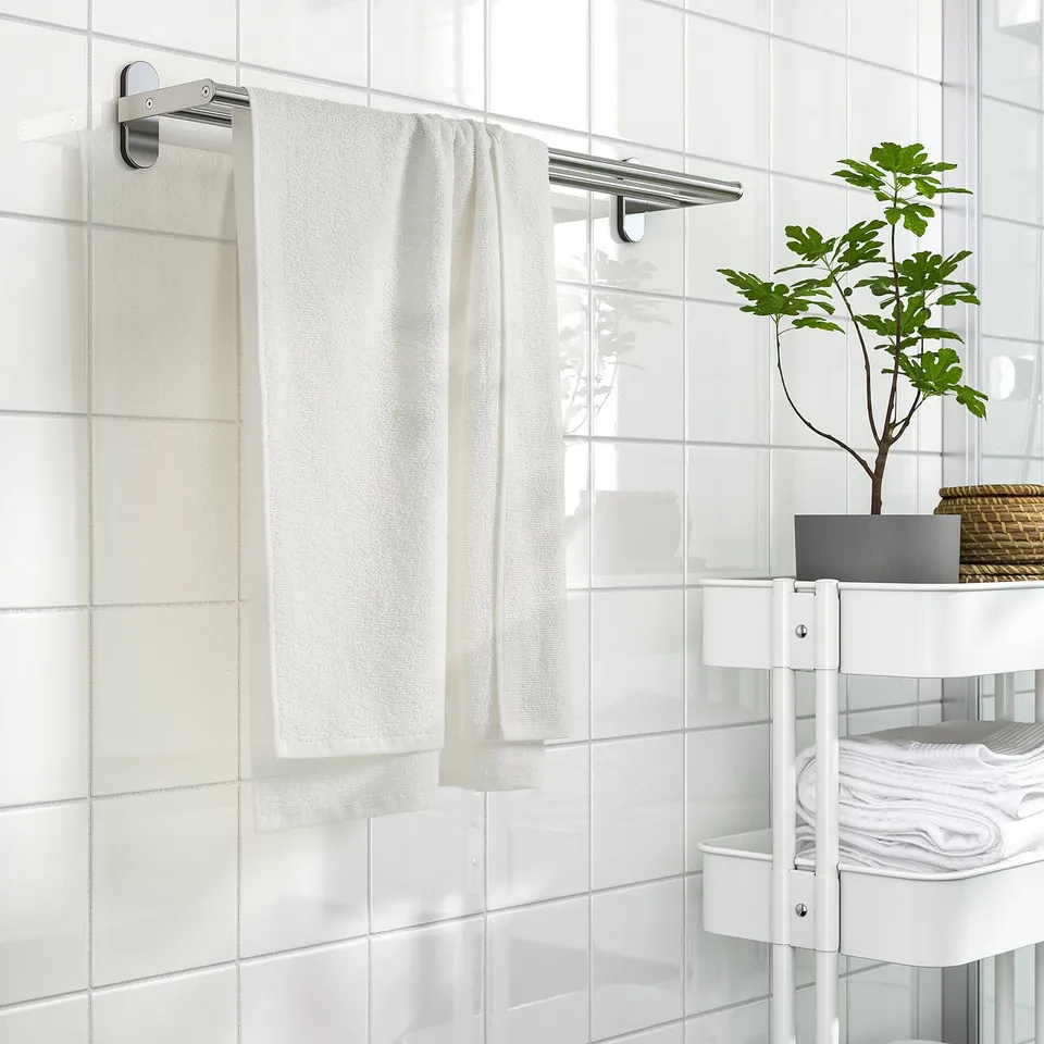 White ludvial towel on steel rack in a bathroom with white tiles and shelving.