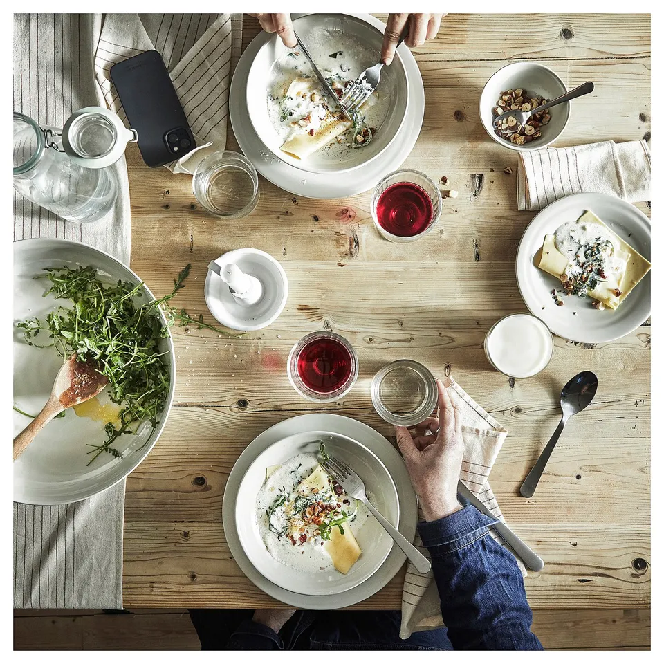 Rustic table with SANDSKÄDDA dinnerware, people enjoying a meal.