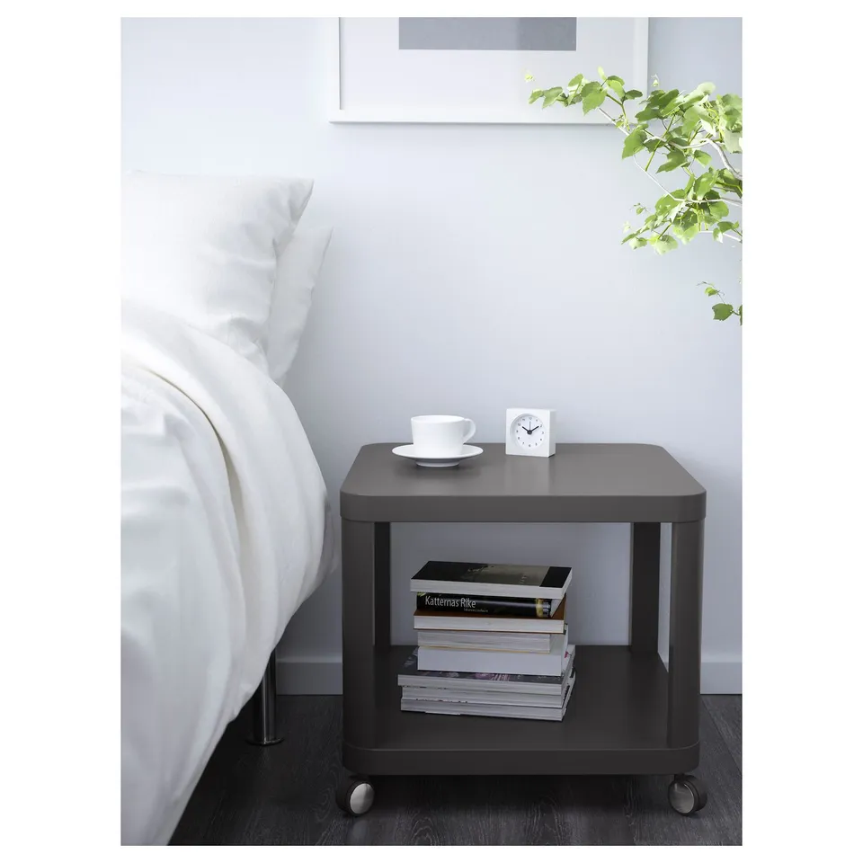 Modern bedside table with casters, holding books and tea set. Functional for small rooms.
