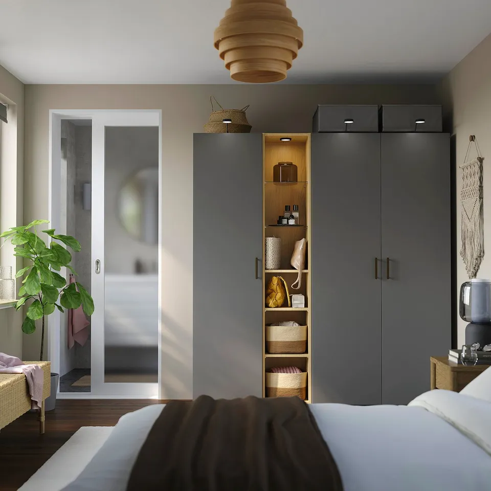 Modern bedroom with dark grey PAX wardrobe, tall plant near glass doors, bed with white & brown covers.