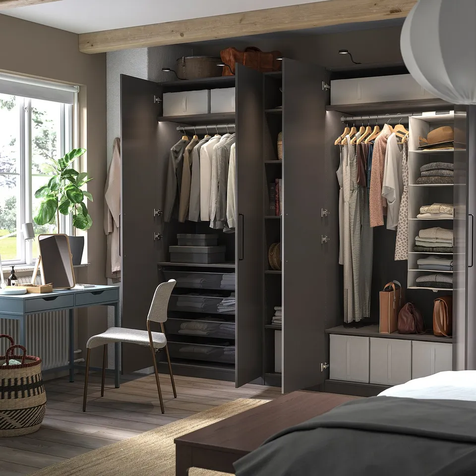 Modern bedroom with black PAX wardrobes, wooden floor, and green desk. Clothes hang and fold neatly.