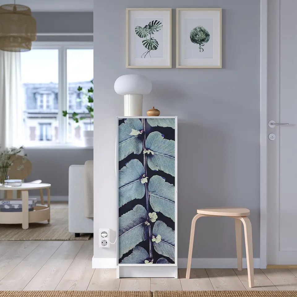 Modern room with HÖGBO glass door, blue floral pattern. Wooden stool, plant pictures, white lamp, and outdoor view.