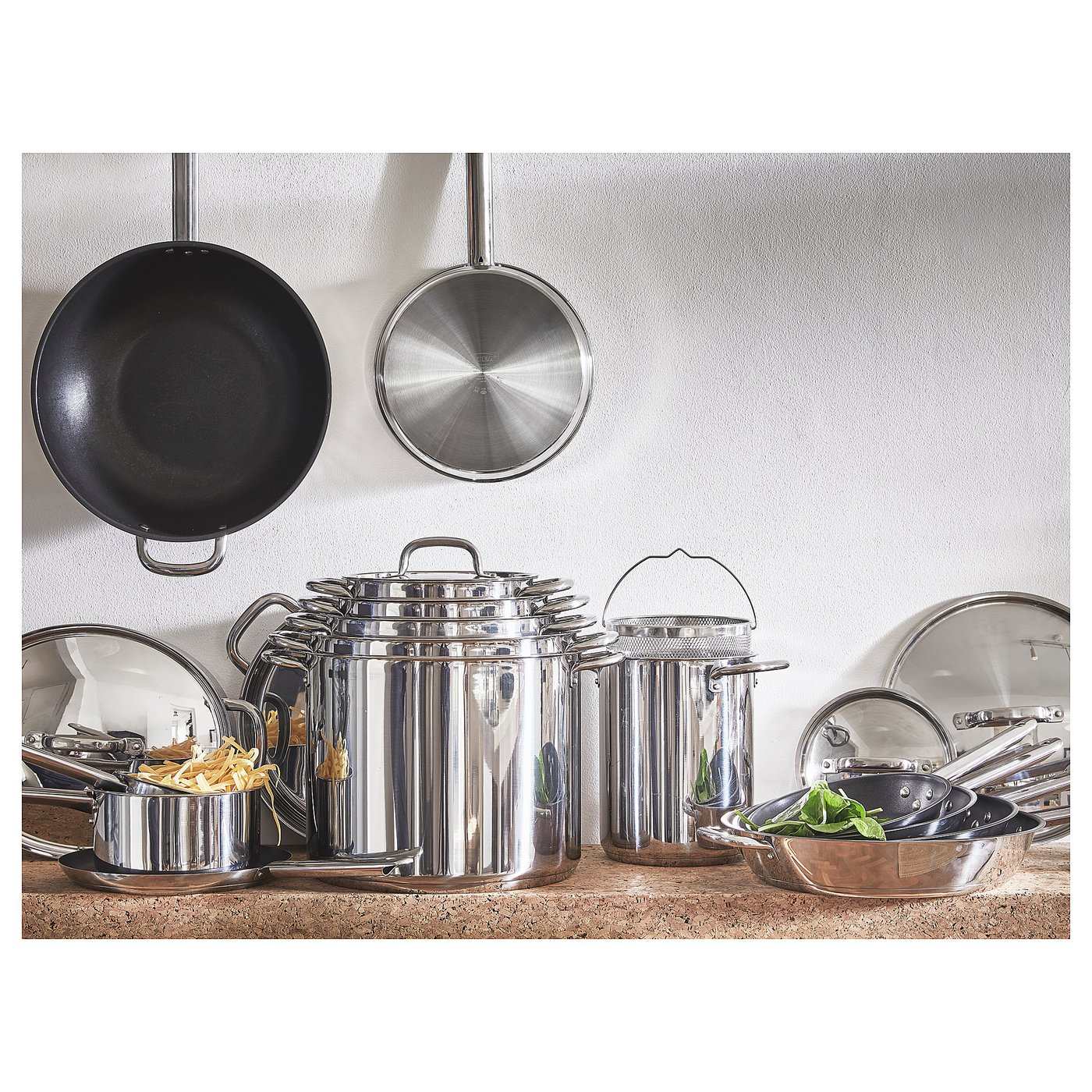 IKEA 365+ kitchenware set: shiny stainless steel cookware including saucepans, frying pans, and strainers; neatly arranged on a counter.