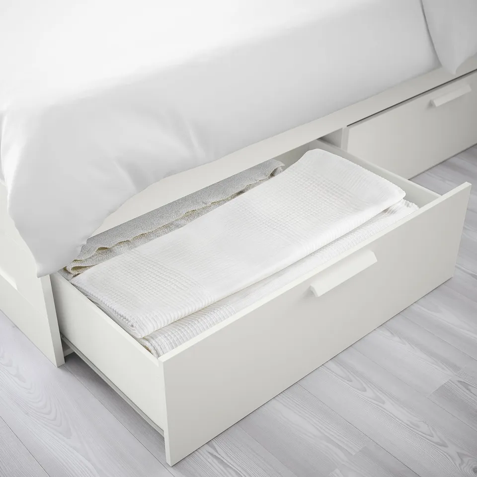 Open white bed drawer showing folded bed linens. Drawer part of compact under-bed storage solution.