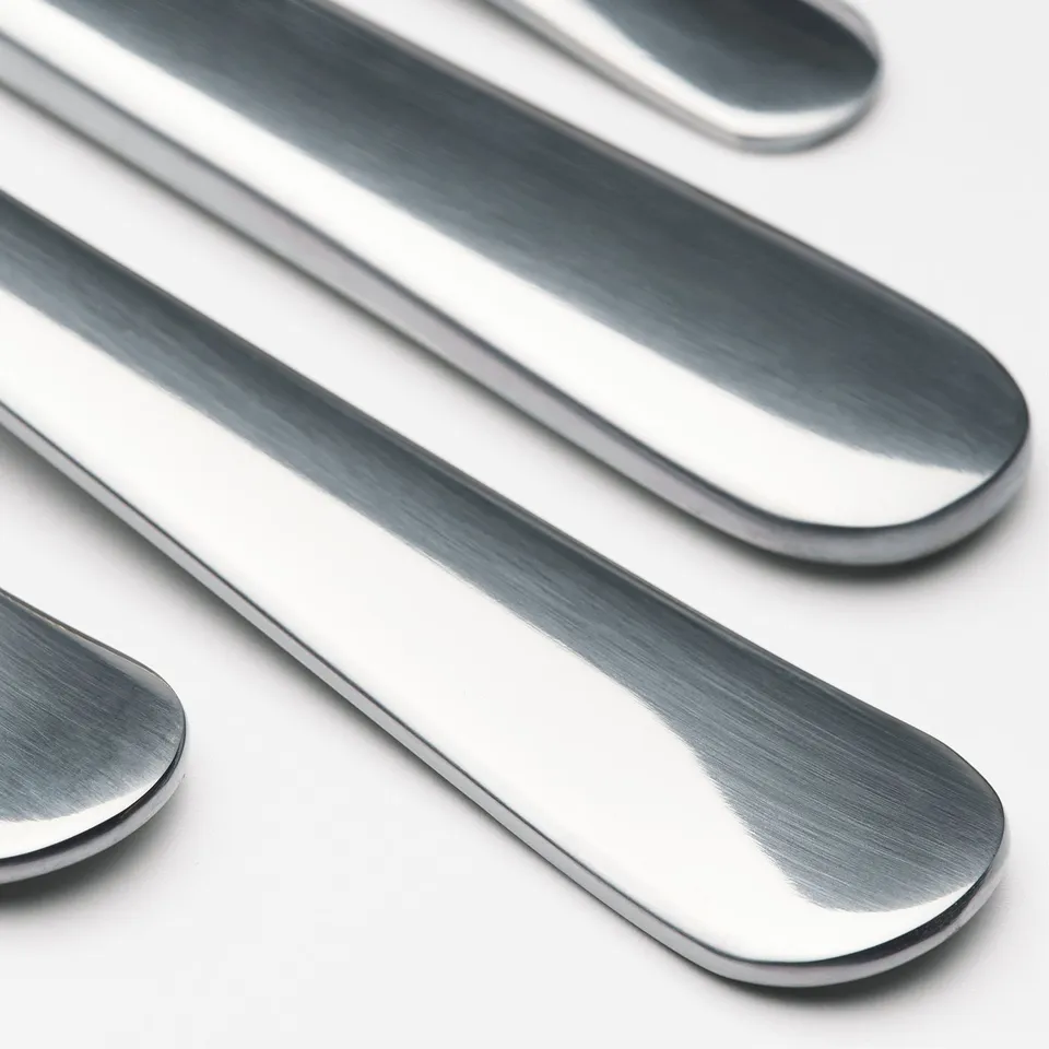 Polished stainless steel cutlery—knife, spoon, fork—neatly arranged on white surface, reflecting light.
