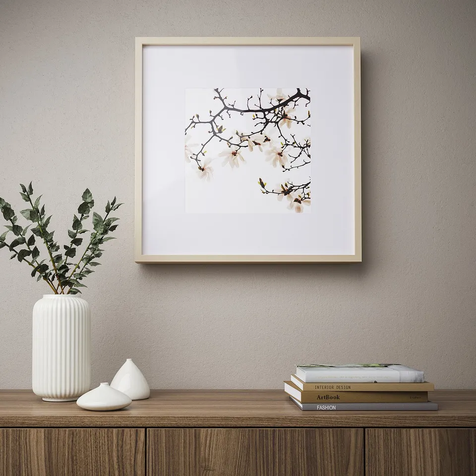 Framed picture of white flowers above shelf with vase, candle, books.
