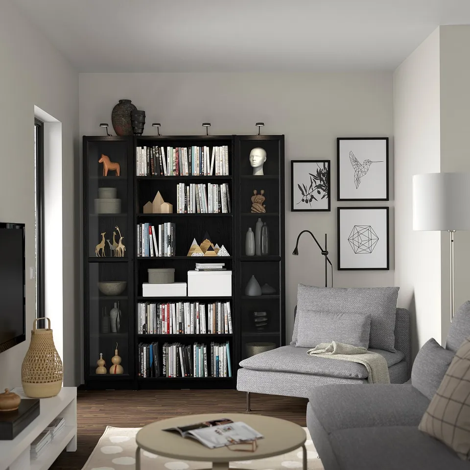 Modern living room with BILLY black bookcases, grey couch, coffee table, and wall art. Large tv on left, books, and decorations on shelves.