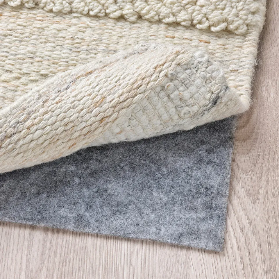 Grey felt rug pad under cream woven wool rug, showing non-slip feature.