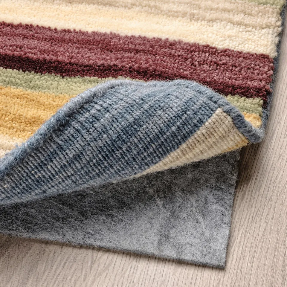 A colourful, striped wool rug folded on a wooden floor, showcasing its thick, handwoven texture and loop pile edge.