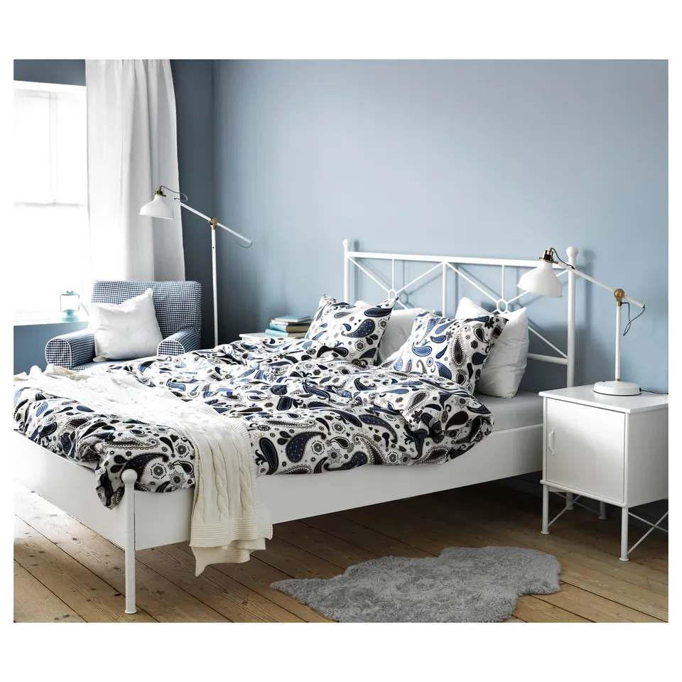 Bedroom with white MUSKEN bedside table, grey rug, patterned bedding on white bed, and blue walls.