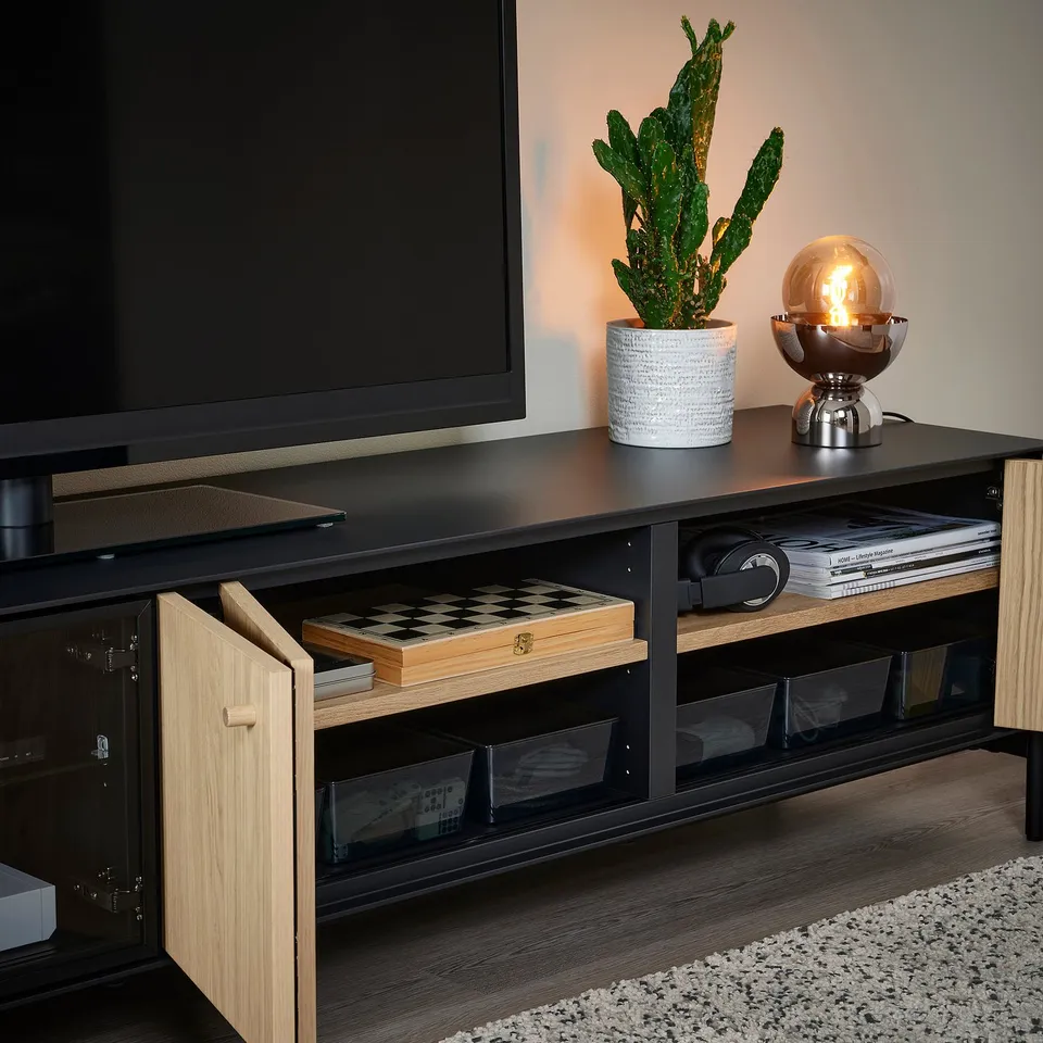 Modern tv stand with glass doors, cable management, chess board, plant, lamp, and open storage.