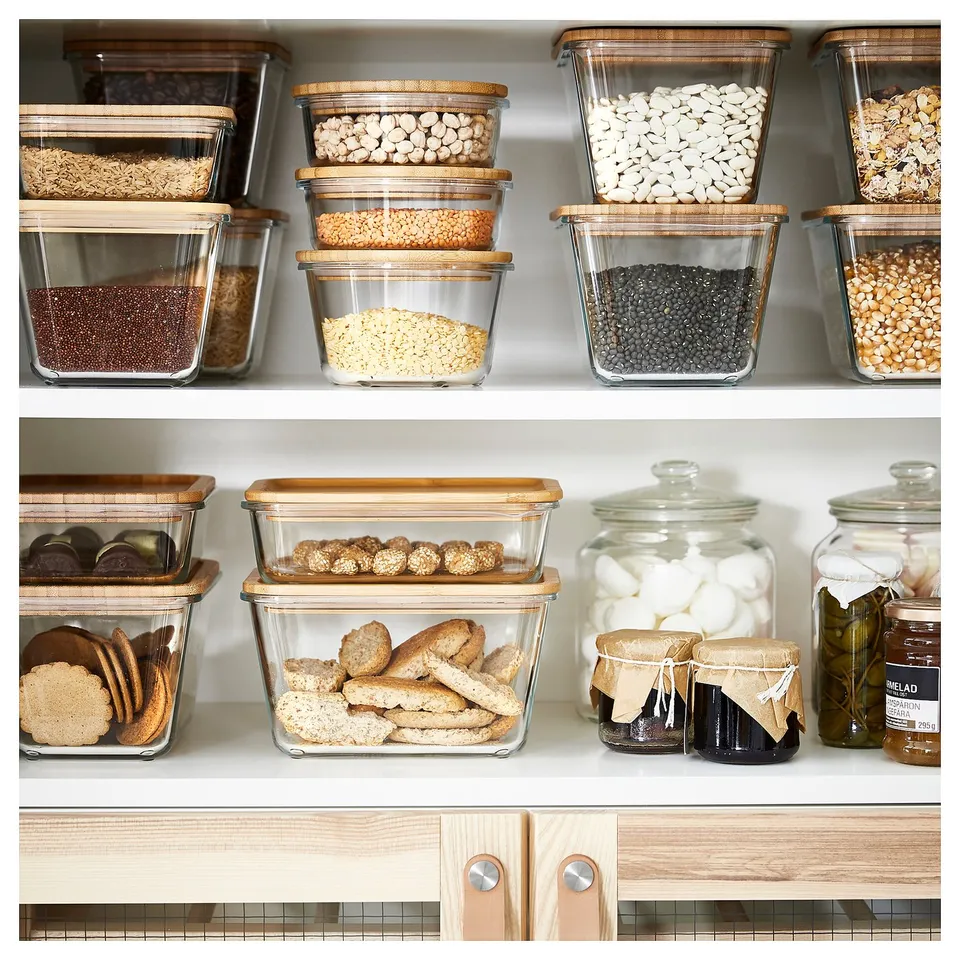 IKEA 365+ clear glass containers with wooden lids, storing various dry foods on wooden shelves.
