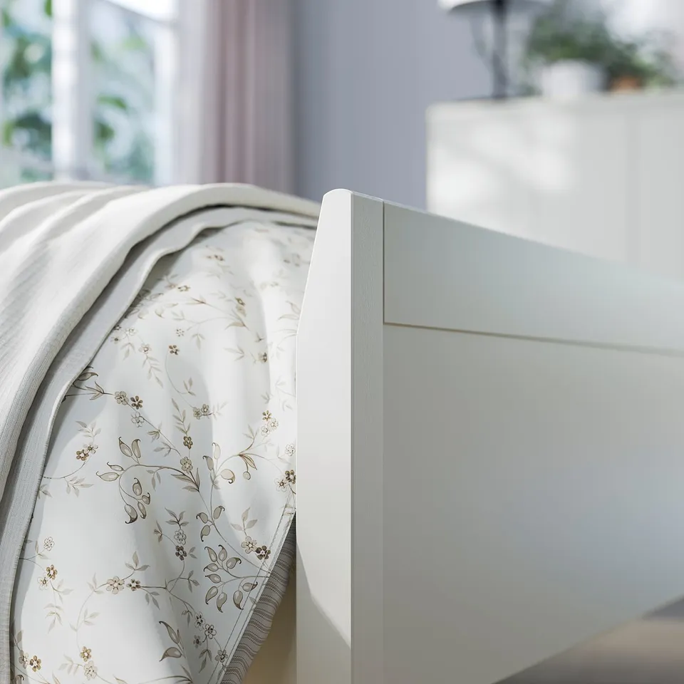 White wooden bed frame, floral patterned bedding, soft blankets, cosy bedroom scene.