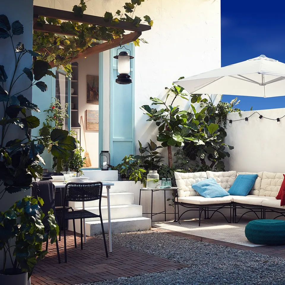 Cosh outdoor space featuring JUTHOLMEN white plastic rattan modular sofa with blue and red cushions, large white umbrella, and potted plants.
