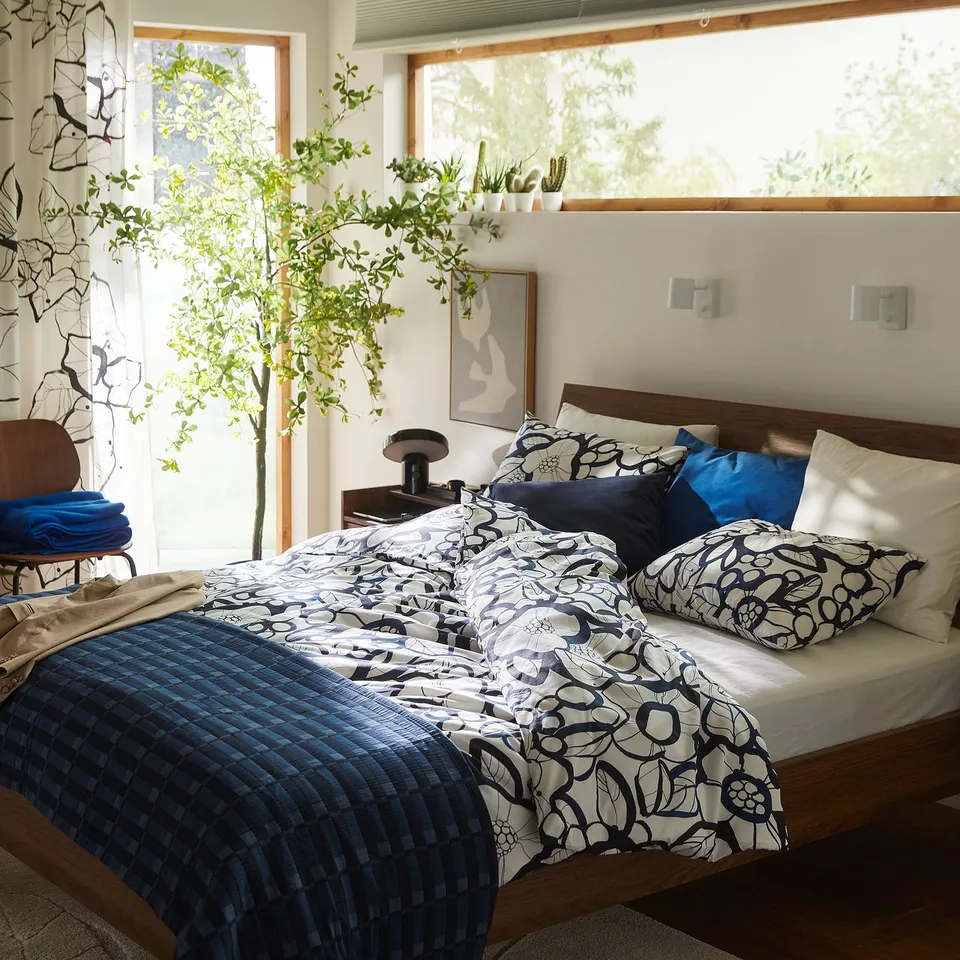 Blue and white floral bedding in large bedroom with tree and window.