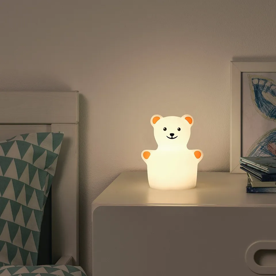 A childrens bedroom with a TÖVÄDER night light, featuring a teddy bear shape, emitting warm light on a bedside table.