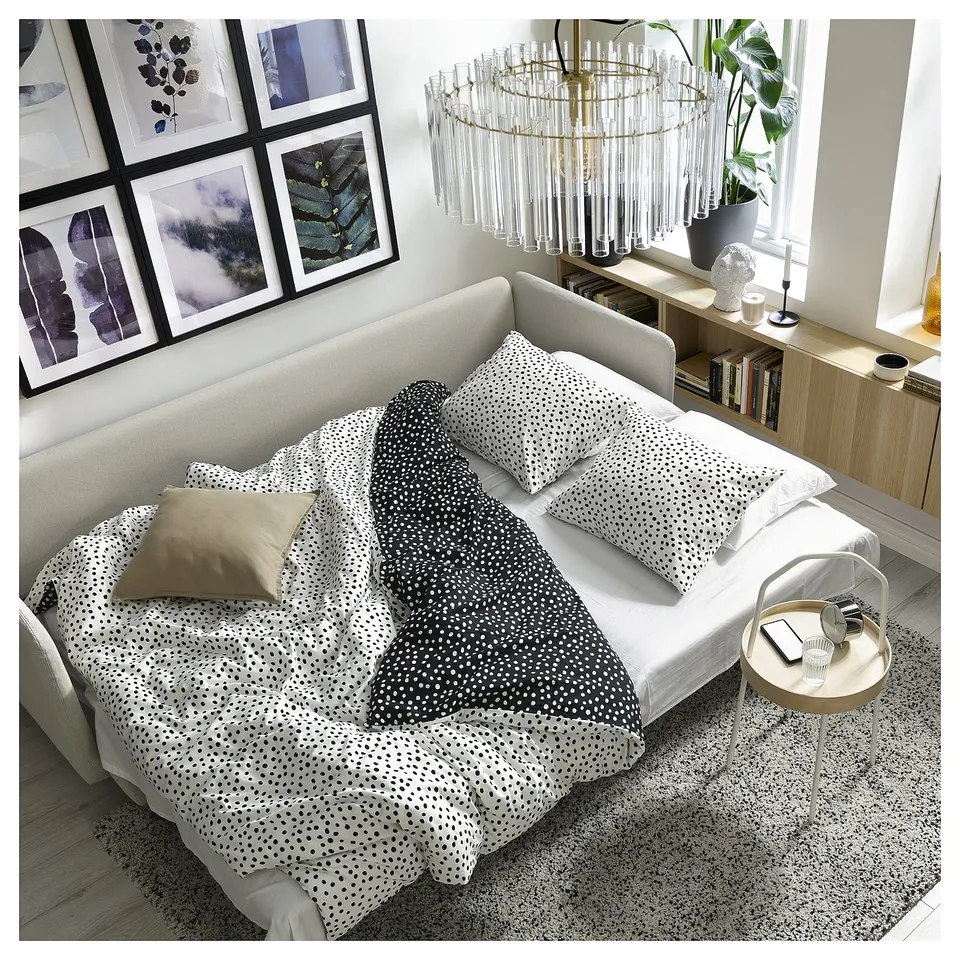 A modern white sofa bed with black dot cushions; sleek design, high legs, loose supportive back cushions, and a spacious layout.