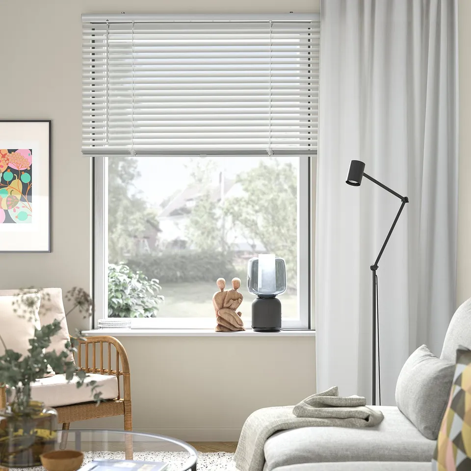 Modern living room with VECKLARFLY blinds, aluminium slats, curtains, chair, lamp, and decor.