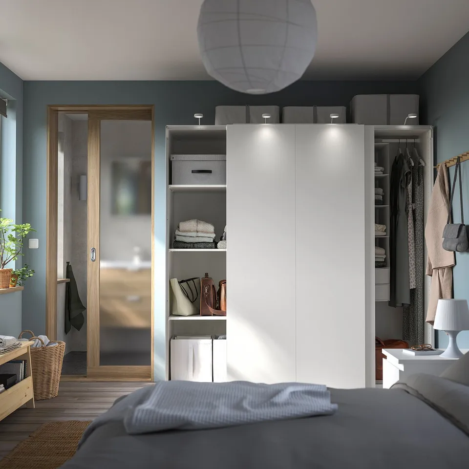Modern bedroom with PAX wardrobes, sliding doors, shelves, and interior lighting. Grey bed, blue walls, cosy space.